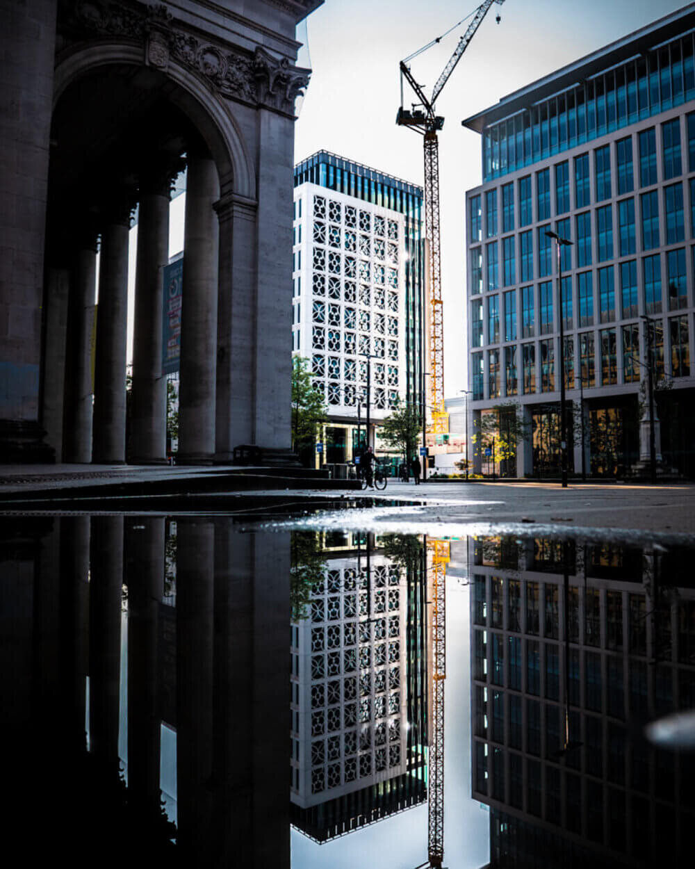 Distant building and Craine perfectly reflected in a puddle at St Peter’s Square