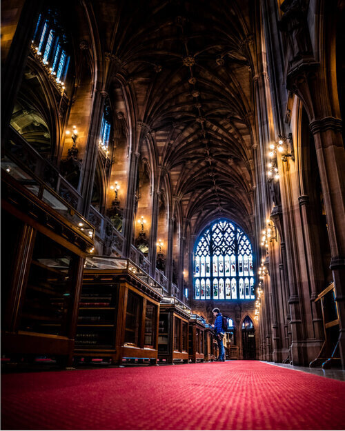 Full room view of John Rylands Library showing visitors exploring and historical architect. 