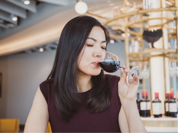 Close-up portrait photography of an asian woman taking a sip of red wine while waiting for her flight in an airport lounge