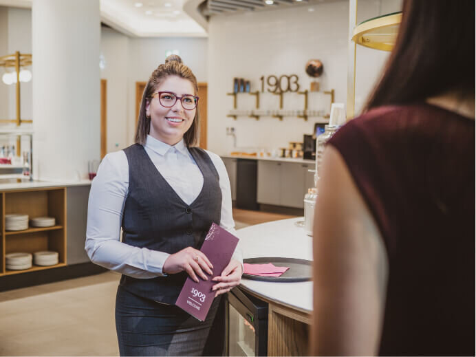 Photography of a waitress smiling while holding a 1903 menu talking to customer