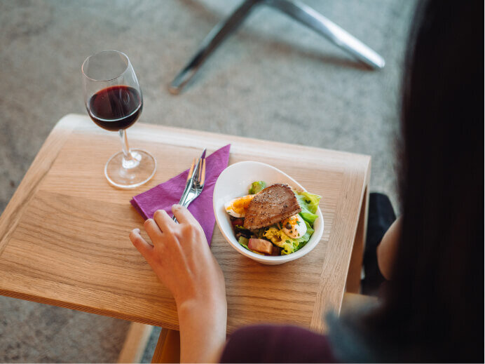 Over the shoulder photography showing a small dish of food and a glass of red wine, inside an airport lounge