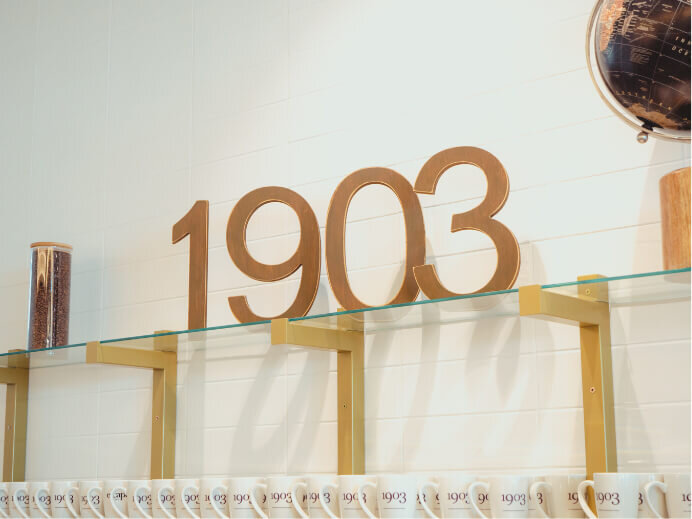 1903 Lounge logo sitting on a glass shelf above branded coffee mugs