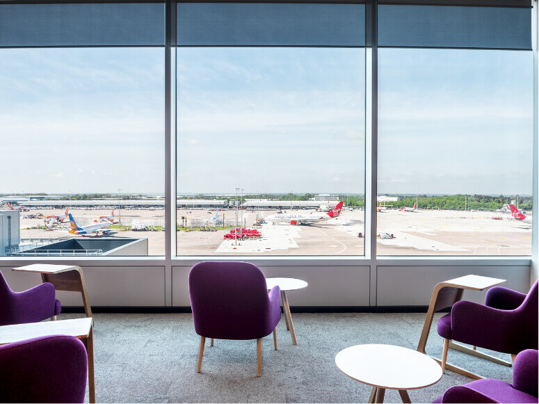 A single purple chair looking out on to Manchester Airports runway with grounded airplanes in the distance 
