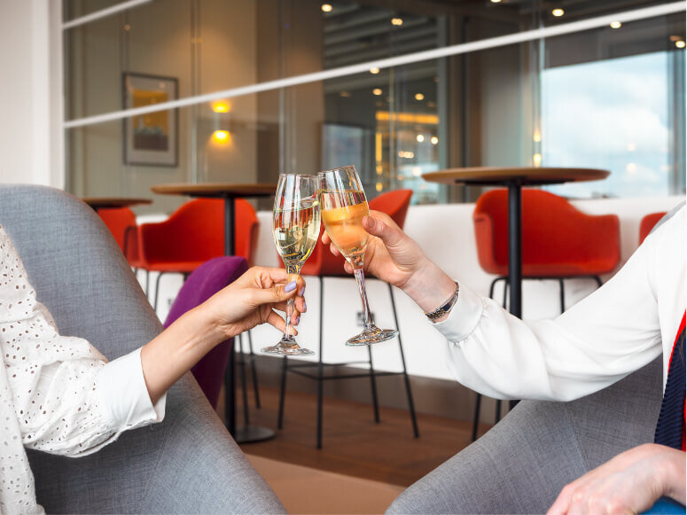 Two women toasting while holding champaign glasses inside Escape Lounges
