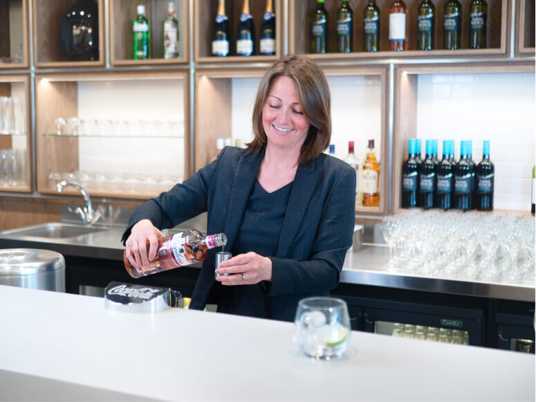 Photography capturing a smiling bar woman pouring a glass of gin