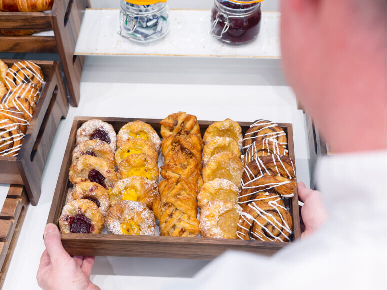 Over the shoulder photography showing a chef placing a box of pastries down on a table