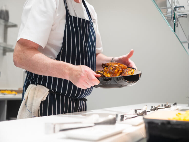 Close up of a chef holding a dish of chicken while restocking a lunch buffet 