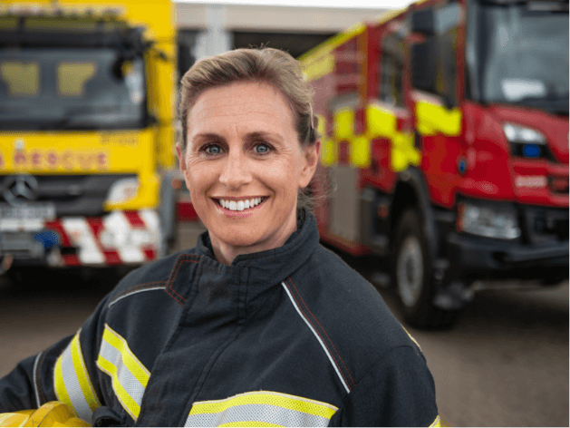 Empowering staff photography showing a female firefighter standing next to two firetrucks