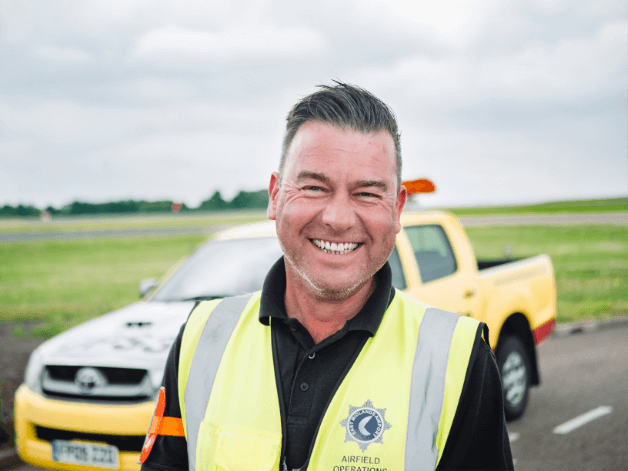 Staff photoshoot on an airport runway showing a smiling man wearing a high vis jacket