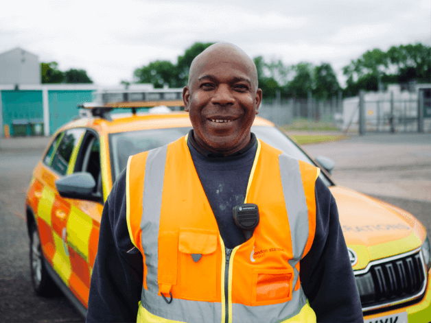 Staff photography showing a smiling airport security guard captured next a car