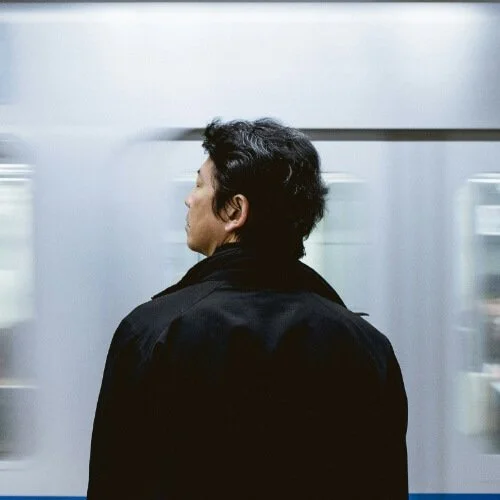Man standing in a subway station with blurred train in the background, showcasing motion blur effect.