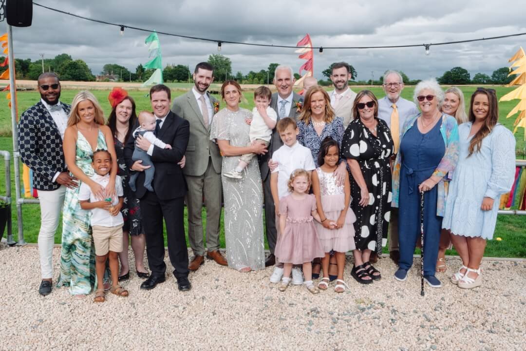 Large family group photo in a garden setting during a wedding celebration