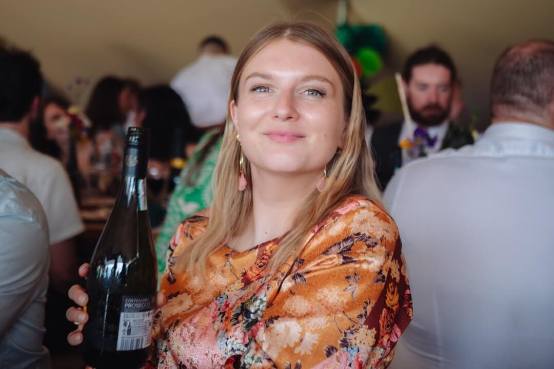 Woman in floral dress holding a wine bottle, smiling at wedding reception
