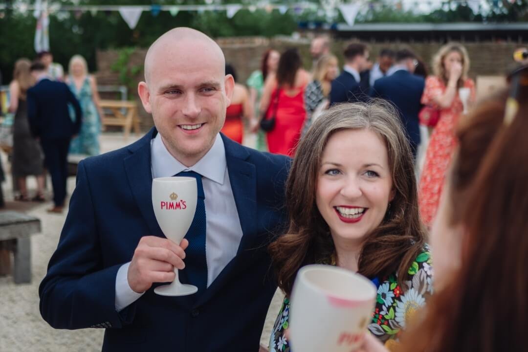Man in suit and woman smiling with drinks at outdoor wedding reception