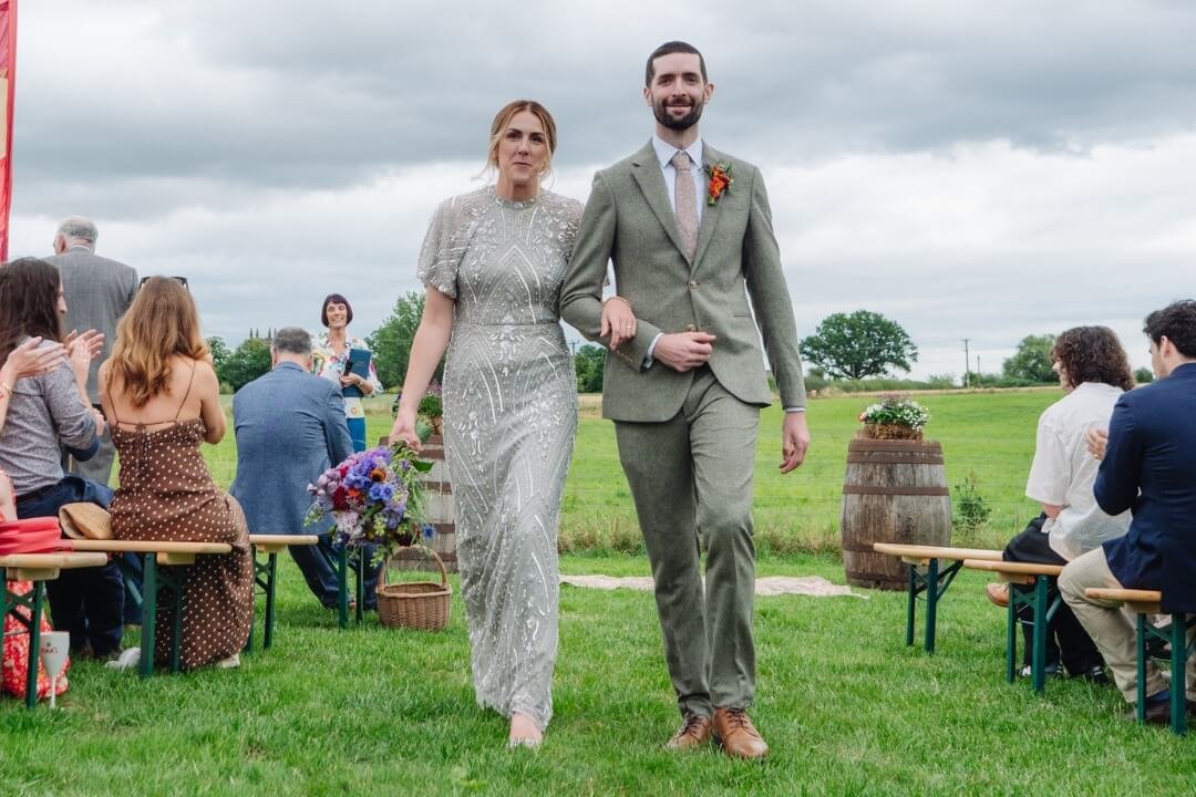 Bride and groom walking arm-in-arm down outdoor wedding aisle