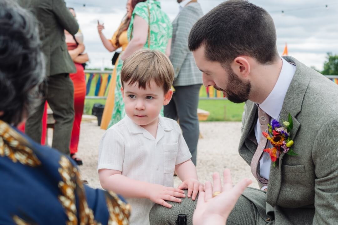 Groom interacting with young boy wearing a floral hat at a wedding reception
