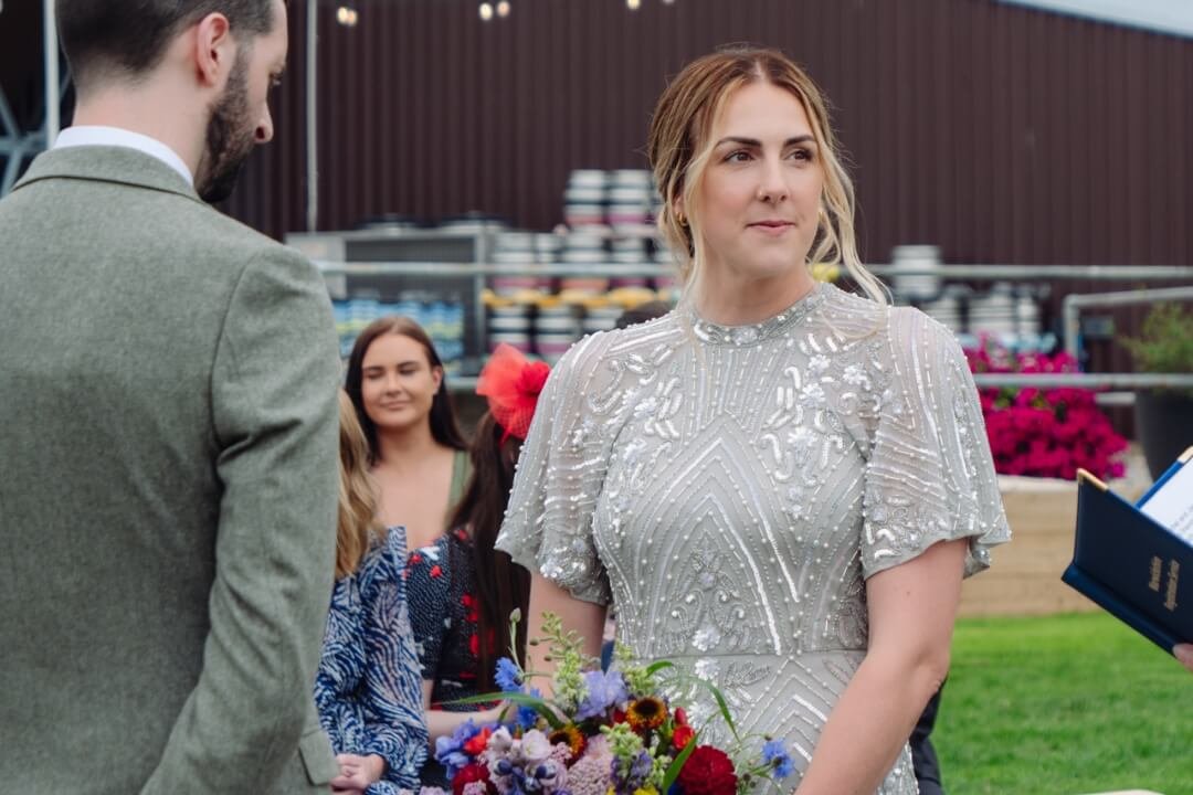 Bride standing with groom during outdoor ceremony, holding bouquet