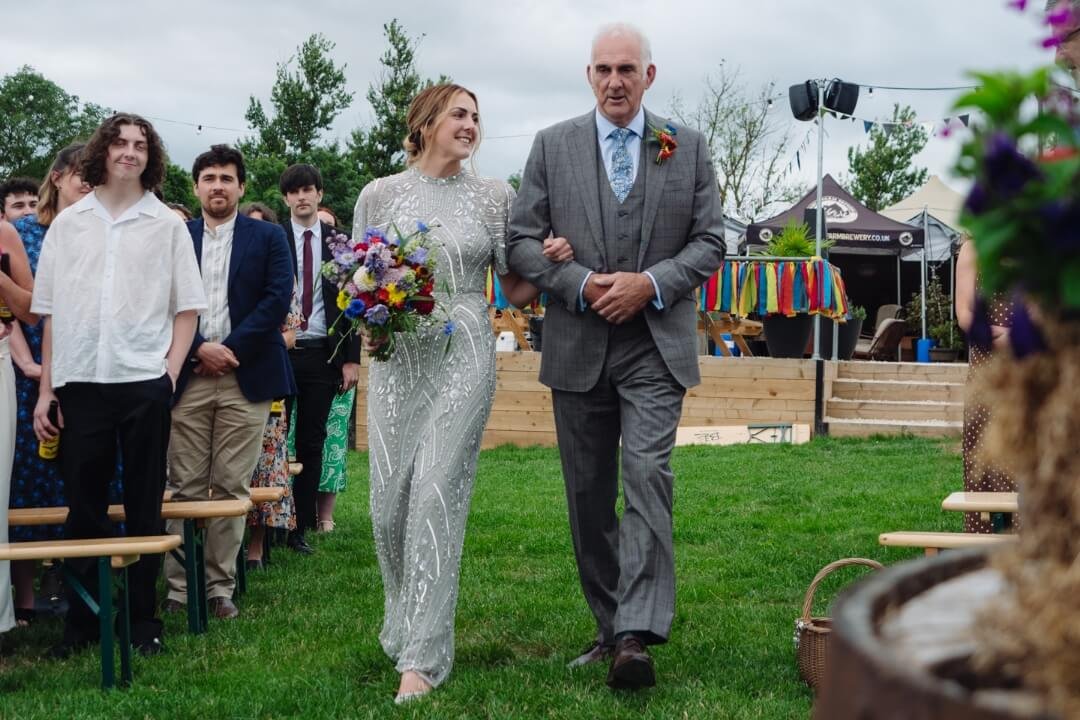 Bride walking down the aisle with father during outdoor wedding ceremony