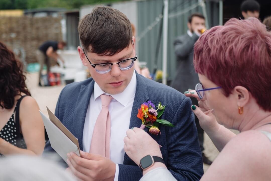 A groom in a suit adjusting his boutonnière with the help of a friend, preparing for his wedding day.