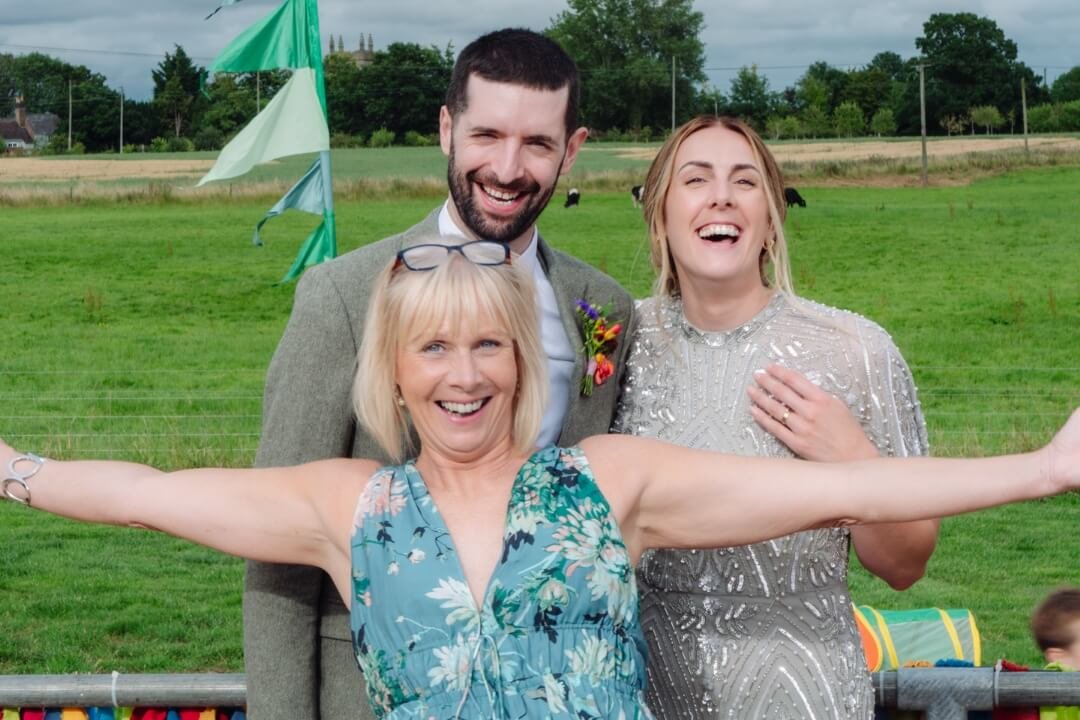 Bride and groom posing with joyful guest at outdoor wedding