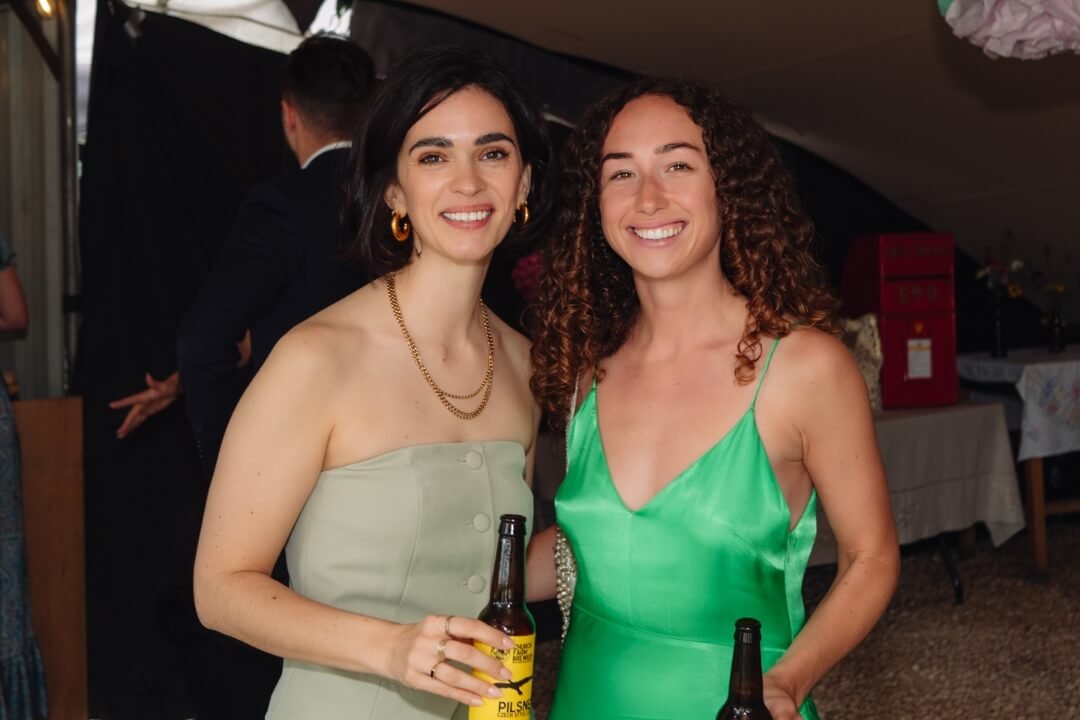 Two women in stylish dresses holding drinks and smiling at wedding