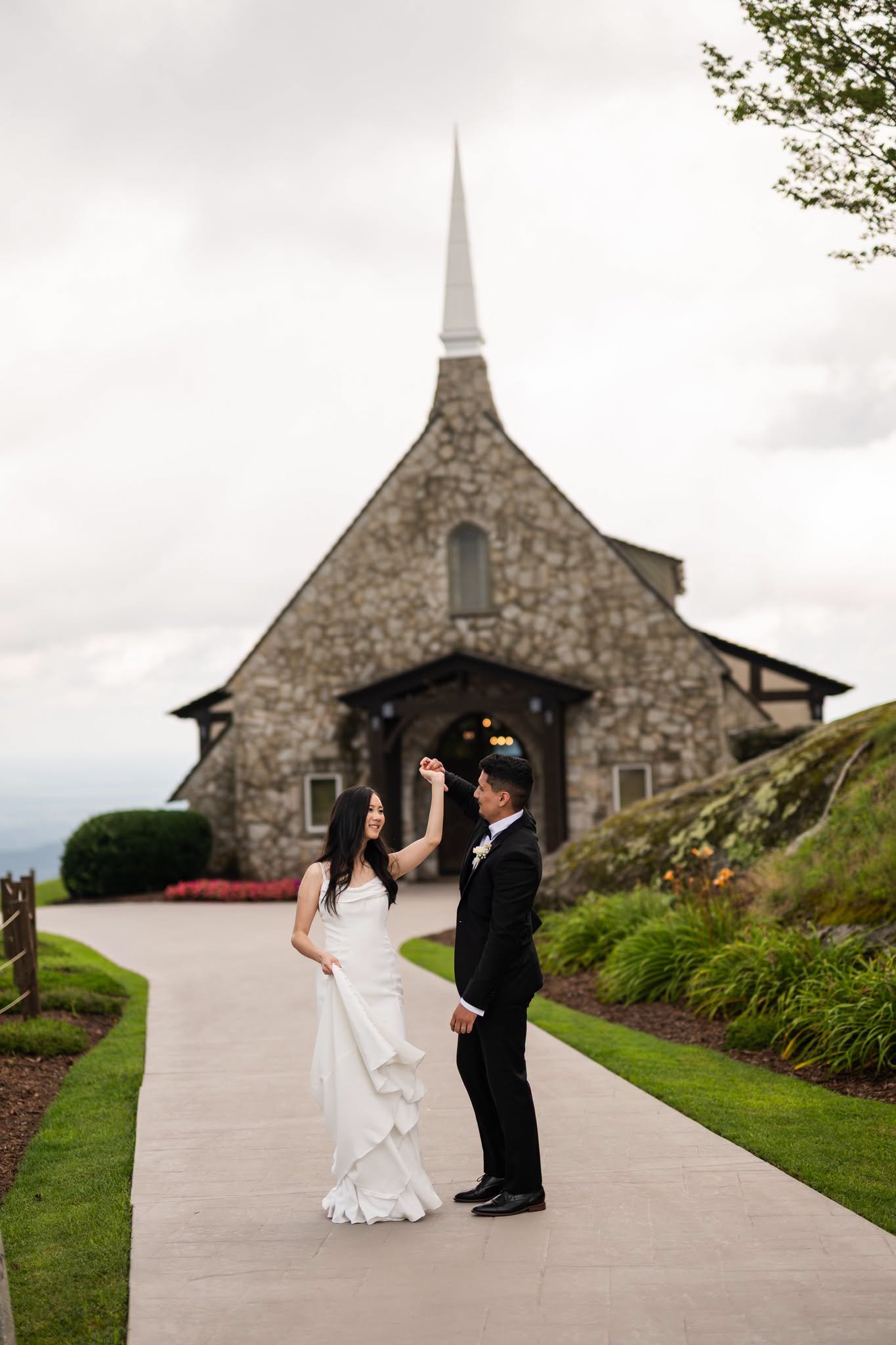 Groom twirling the smiling bride on the walkway in front of the stone chapel at The Cliffs at Glassy.