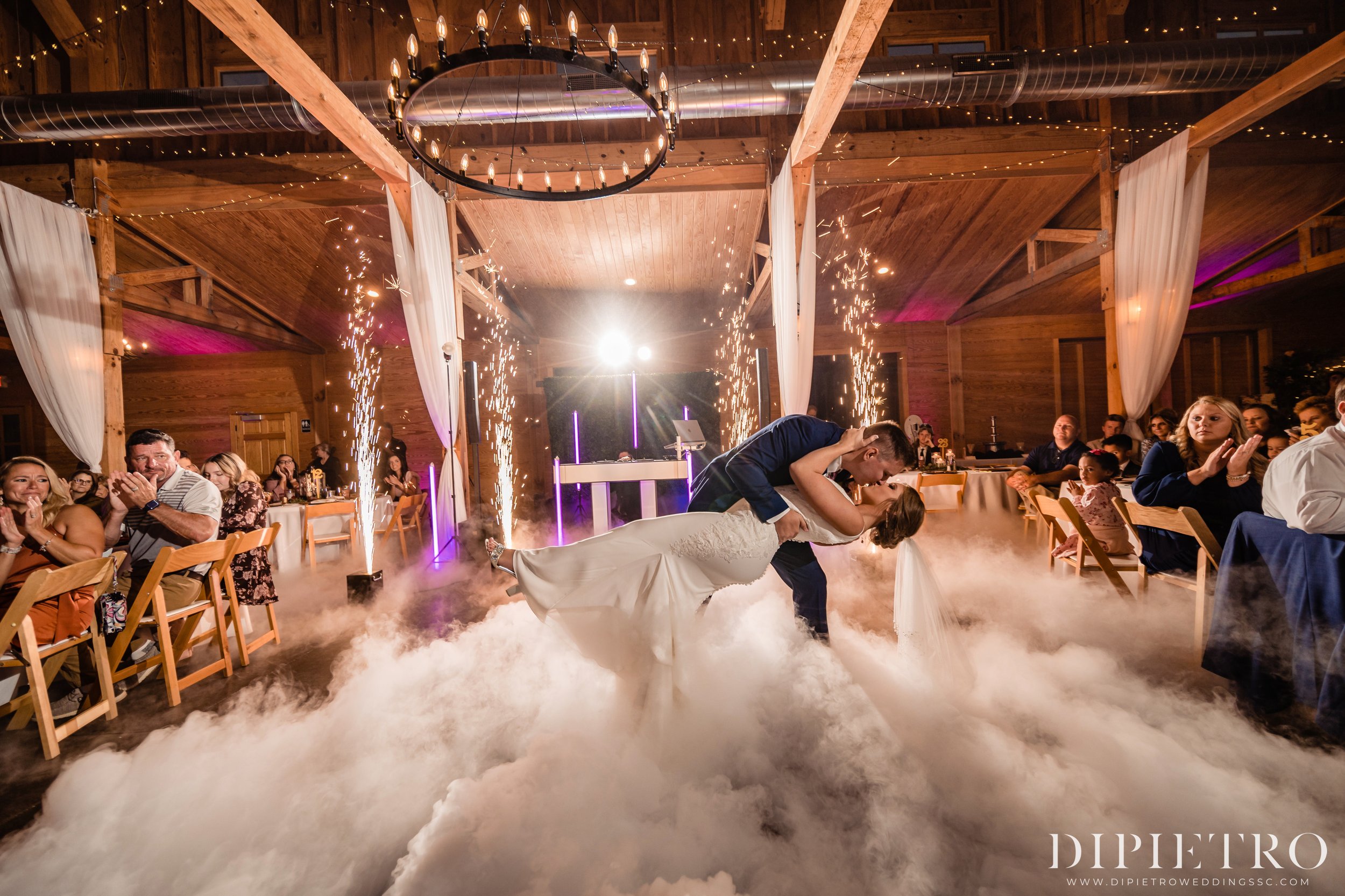 Groom dipping and kissing the bride during their first dance at Southwind Ranch, surrounded by low-lying fog, sparkling fountains, and applauding guests