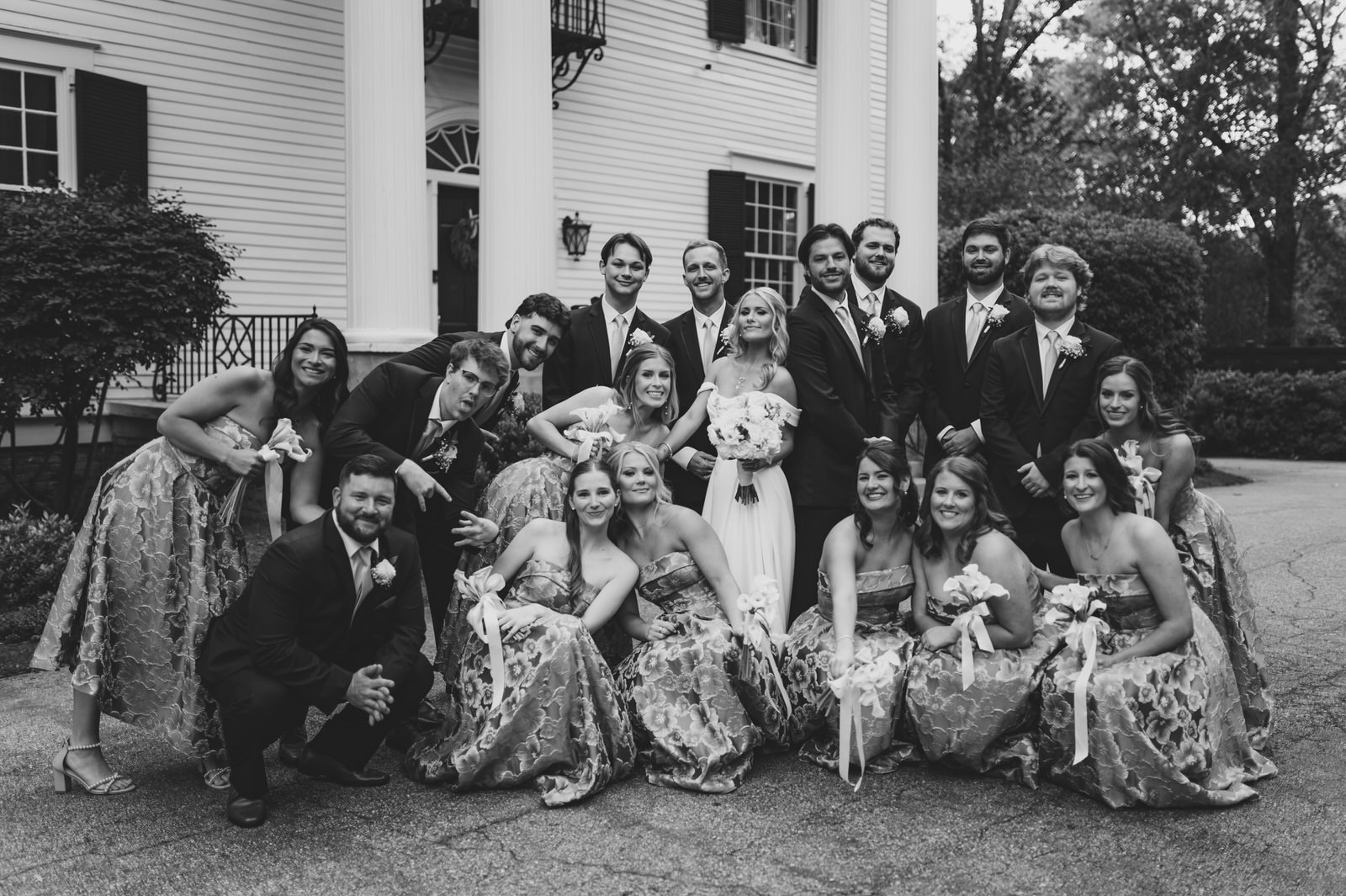 Black and white wedding party portrait with the bride, groom, bridesmaids, and groomsmen outside Duncan Estate’s white-columned house in Spartanburg, SC.