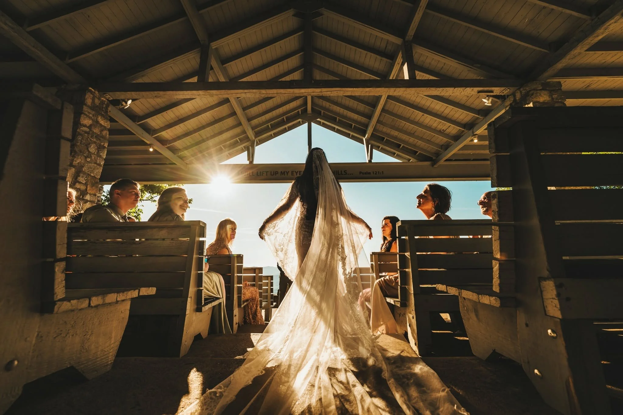 Bride viewed from behind in the aisle at Pretty Place Chapel, with sunlight illuminating her long lace veil as guests look toward her.