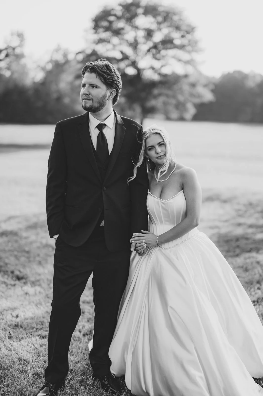 Black and white portrait of a bride resting her head on the groom’s shoulder and holding his hand in a field at The Barn at Sitton Hill.