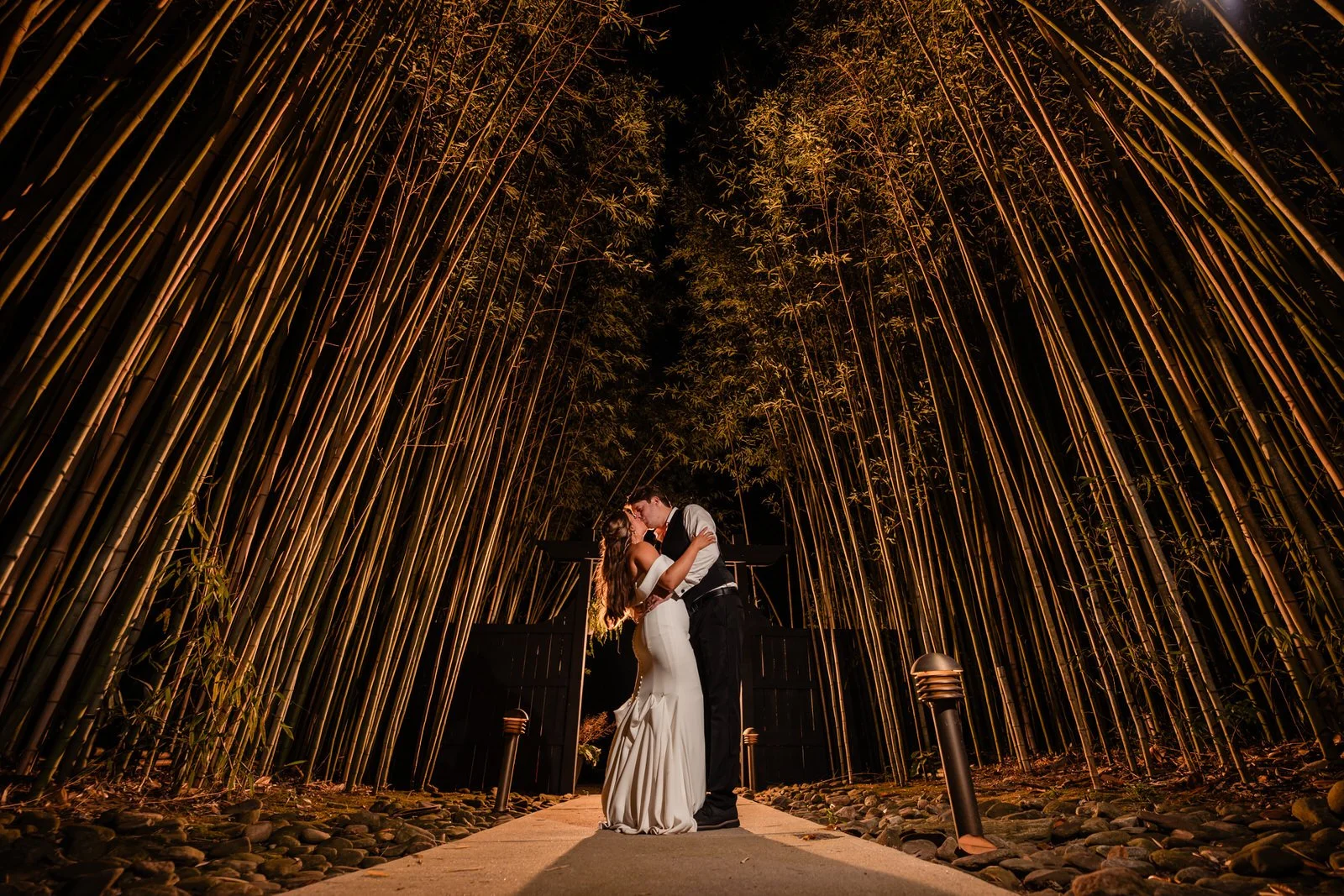 Bride and groom kissing at night on Duncan Estate’s bamboo-lined pathway in Spartanburg, SC, surrounded by warm golden lighting.