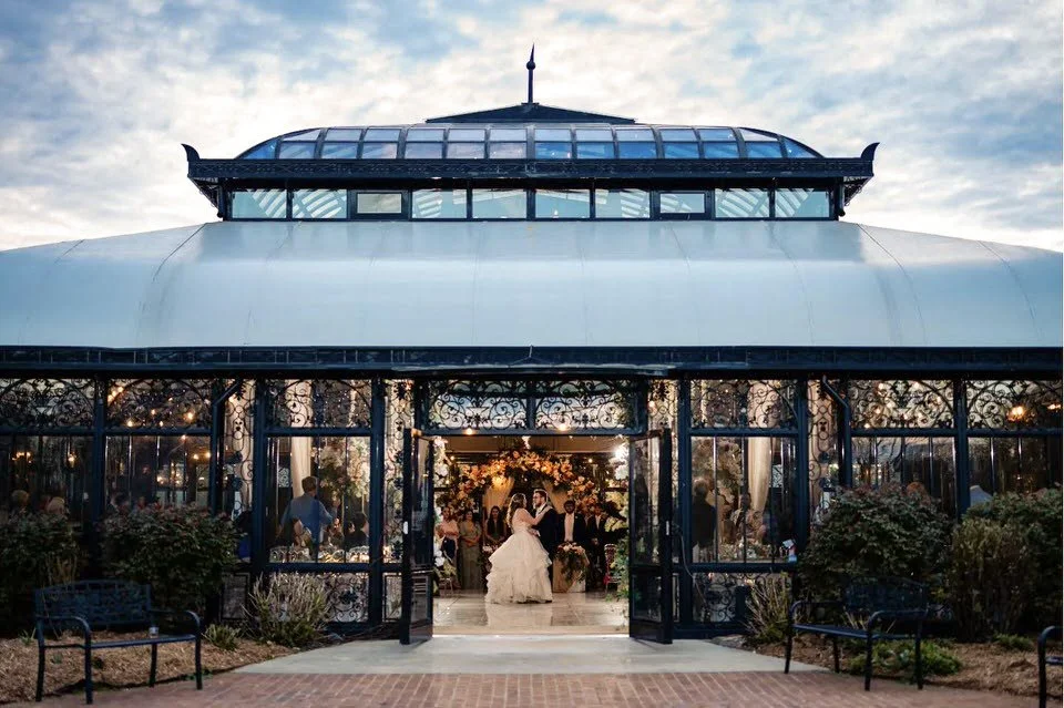 Bride and groom dancing inside Edinburgh West’s glass conservatory, viewed through its open doors beneath a cloudy evening sky.