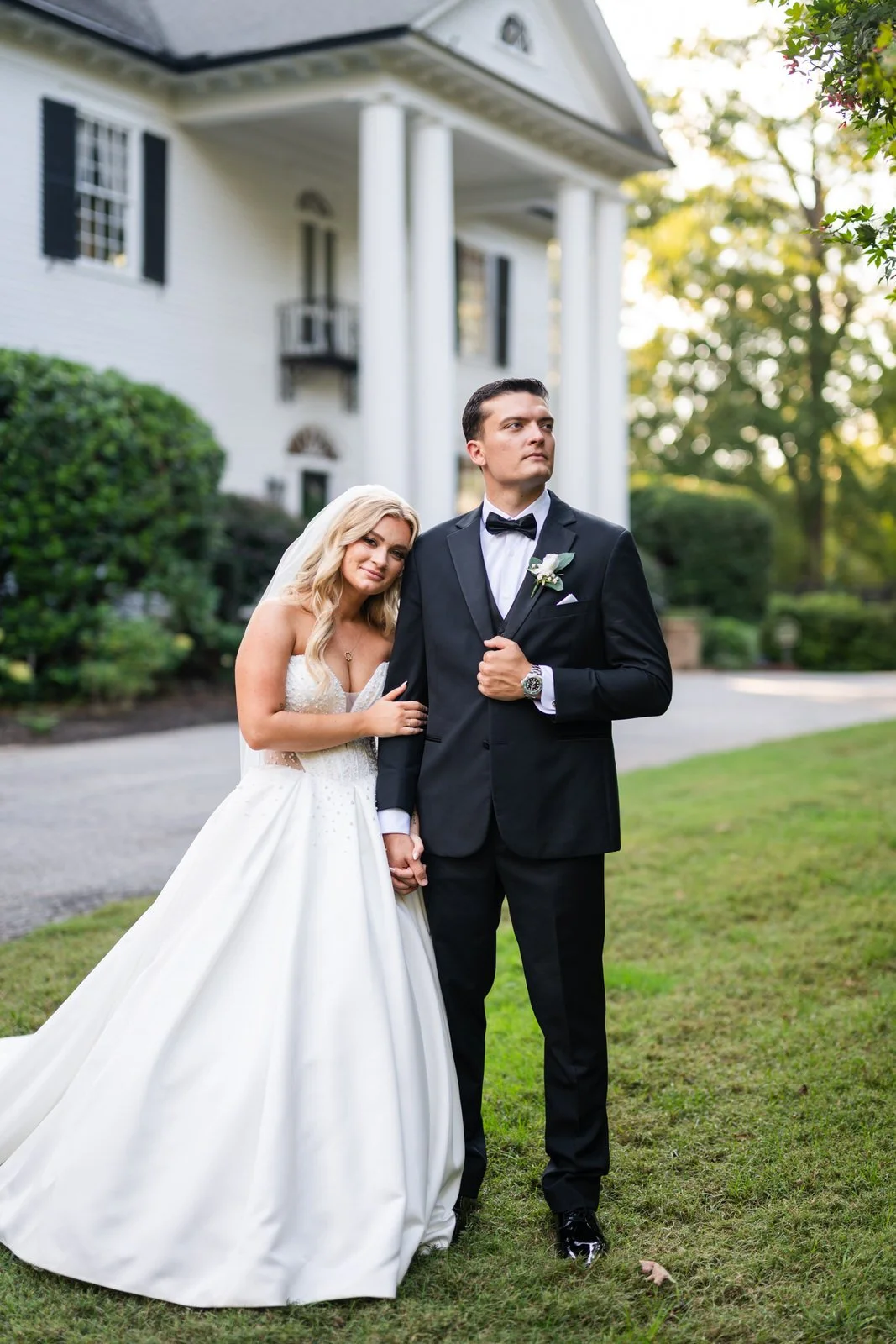 Bride resting her head on the groom’s shoulder while holding hands on the lawn outside Duncan Estate’s white-columned house in Spartanburg, SC.