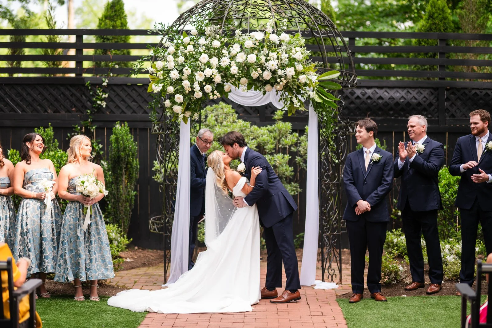Bride and groom sharing their first kiss beneath a white-flower-covered gazebo during an outdoor ceremony at Duncan Estate in Spartanburg, SC.