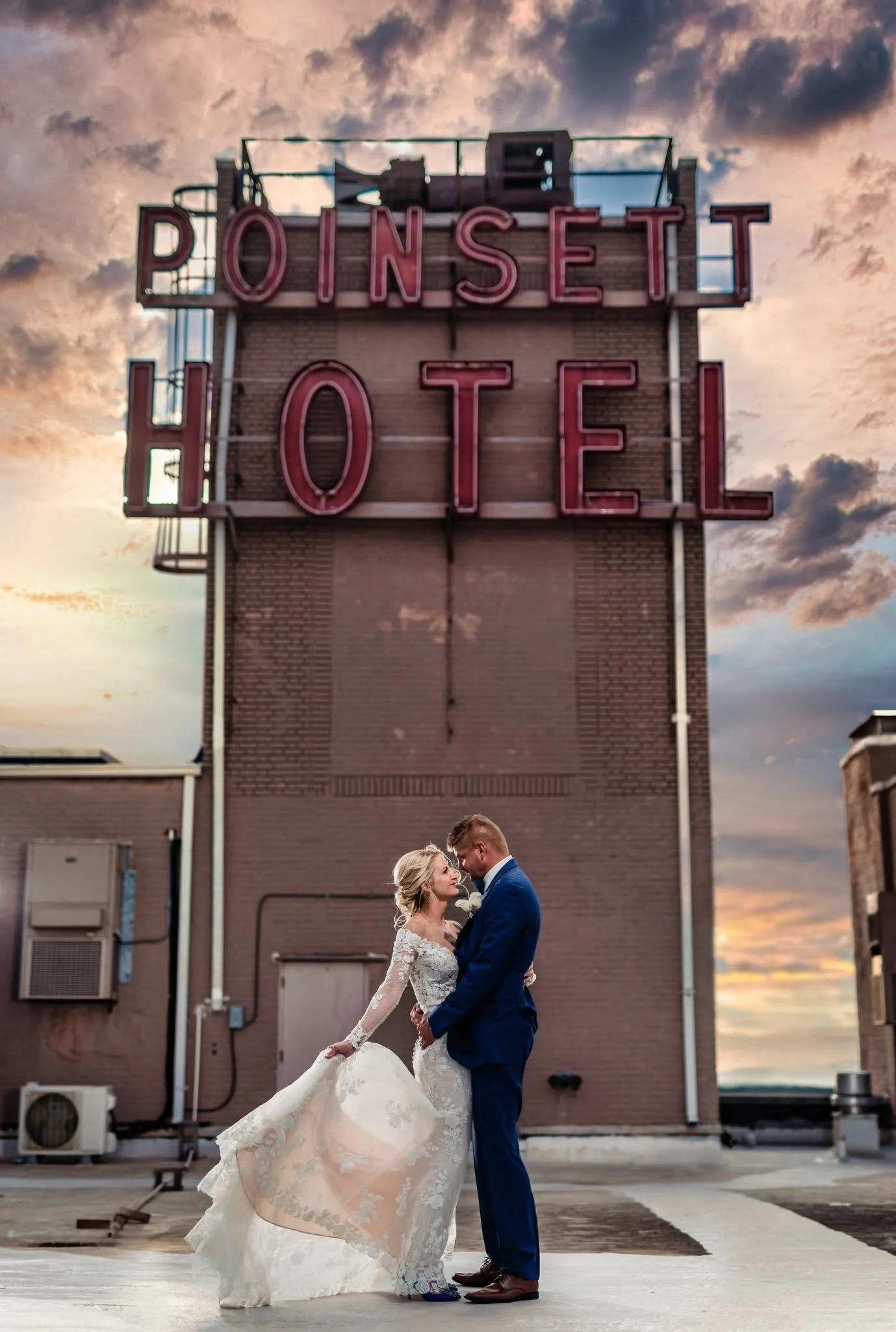 Bride and groom embracing on the rooftop beneath the Poinsett Hotel sign at The Westin Poinsett in Greenville, with sunset clouds behind them.
