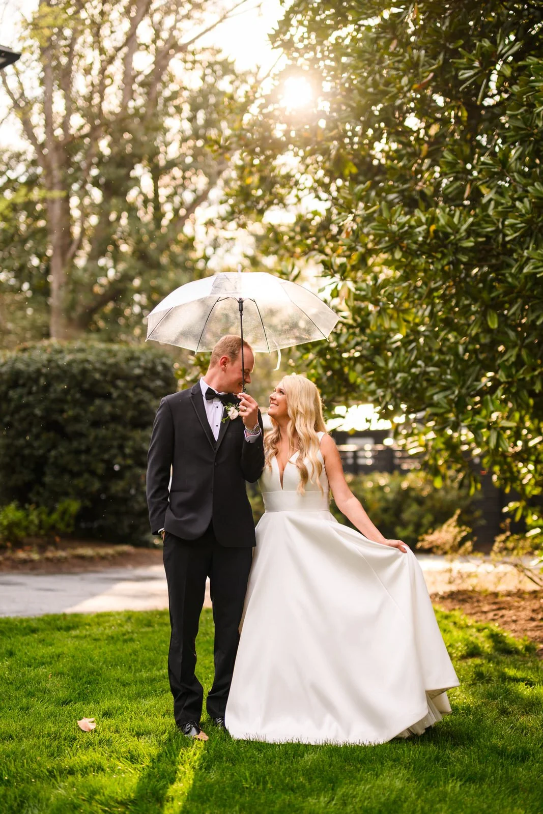 Bride and groom smiling beneath a clear umbrella on Duncan Estate’s lawn, with sunlight filtering through the trees in Spartanburg, SC.