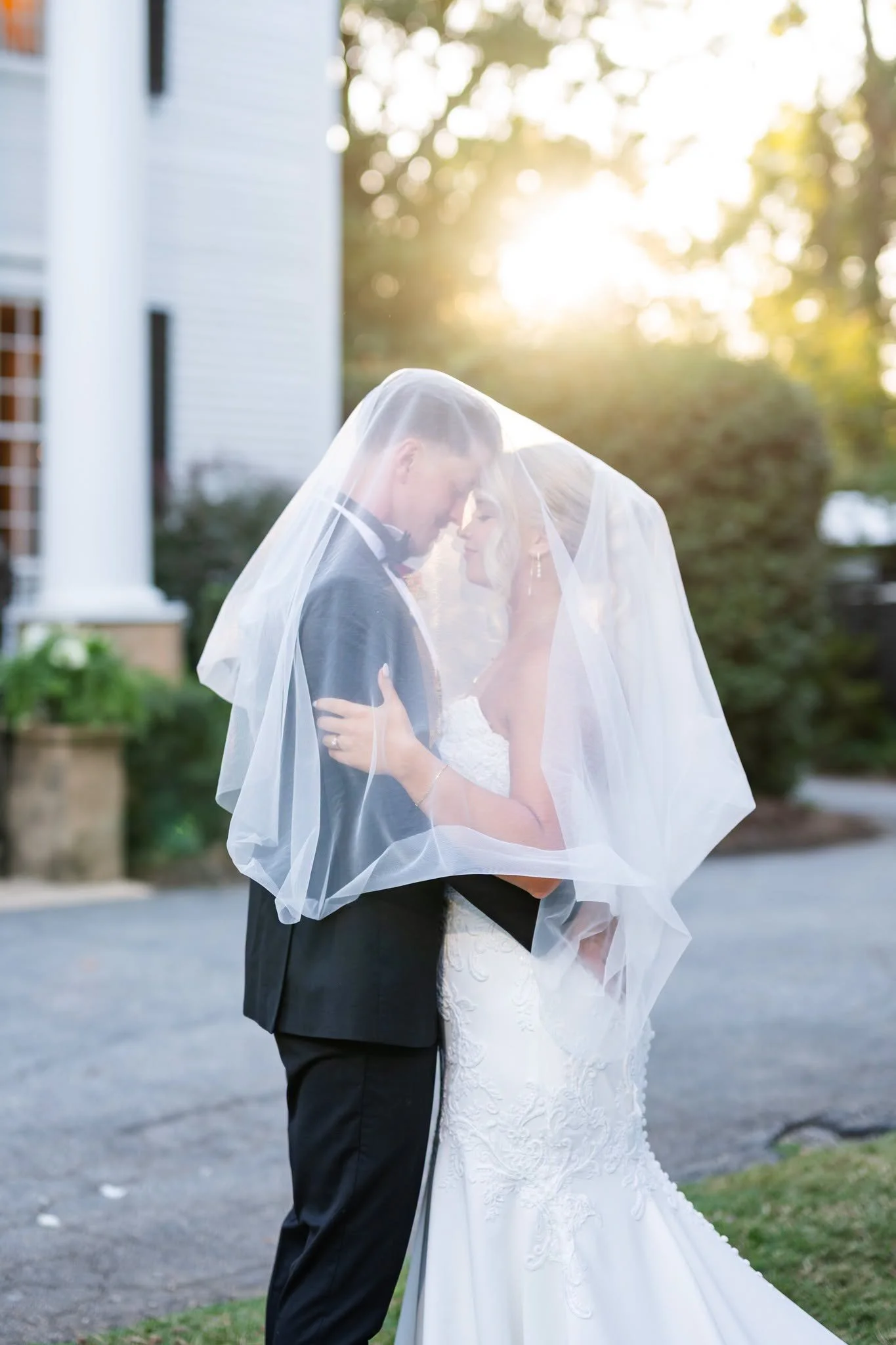 Bride and groom embracing beneath her veil in golden evening light outside the historic house at Duncan Estate in Spartanburg, South Carolina.