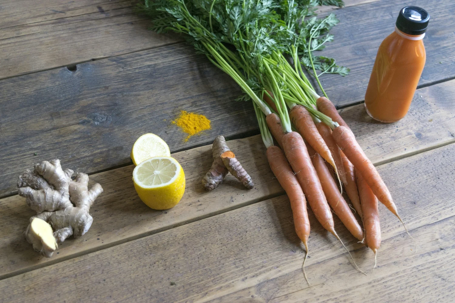 Carrots with their greens, fresh ginger root, turmeric and a halved lemon on a wooden table