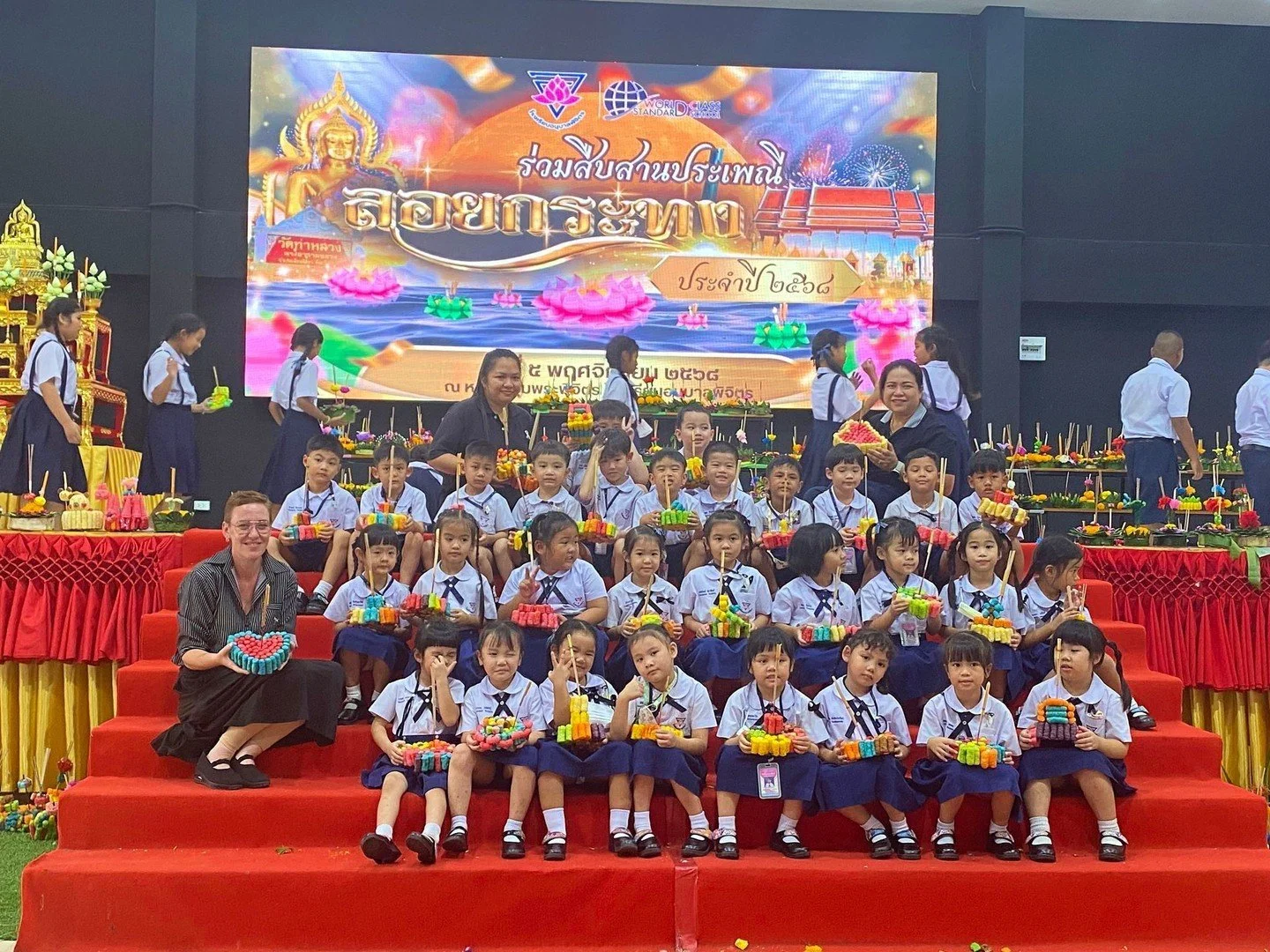 Loy Krathong magic at school just reached a whole new level! 

Teacher Sam gathered her little ones on stage, each proudly holding their handmade krathong, smiles glowing brighter than the candles inside.  One big group photo under the colorful light