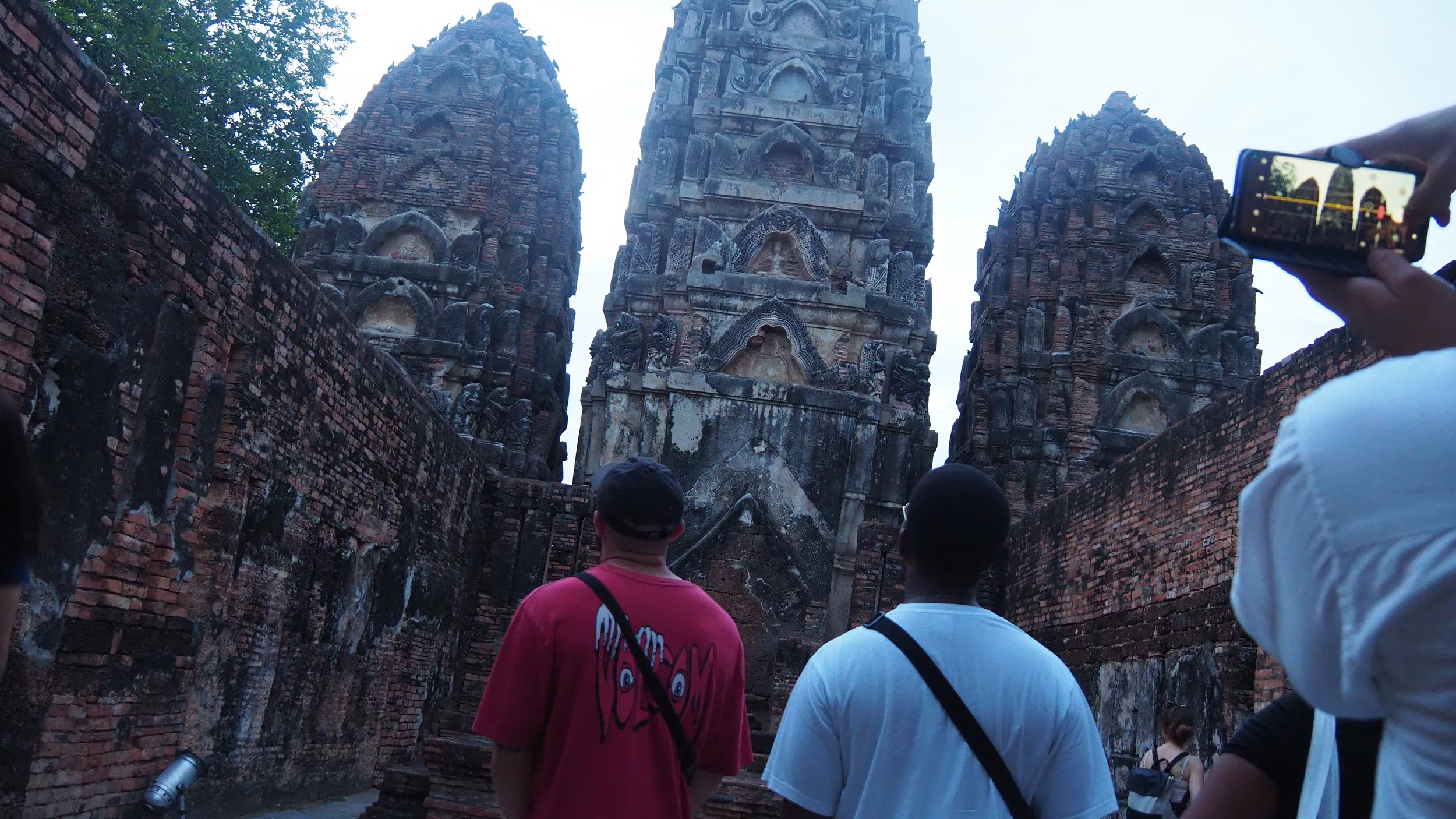 Kids English Thailand teachers standing in front of ancient temple ruins made of brick and stone, with three tall, pointed towers, in a historical archaeological site.