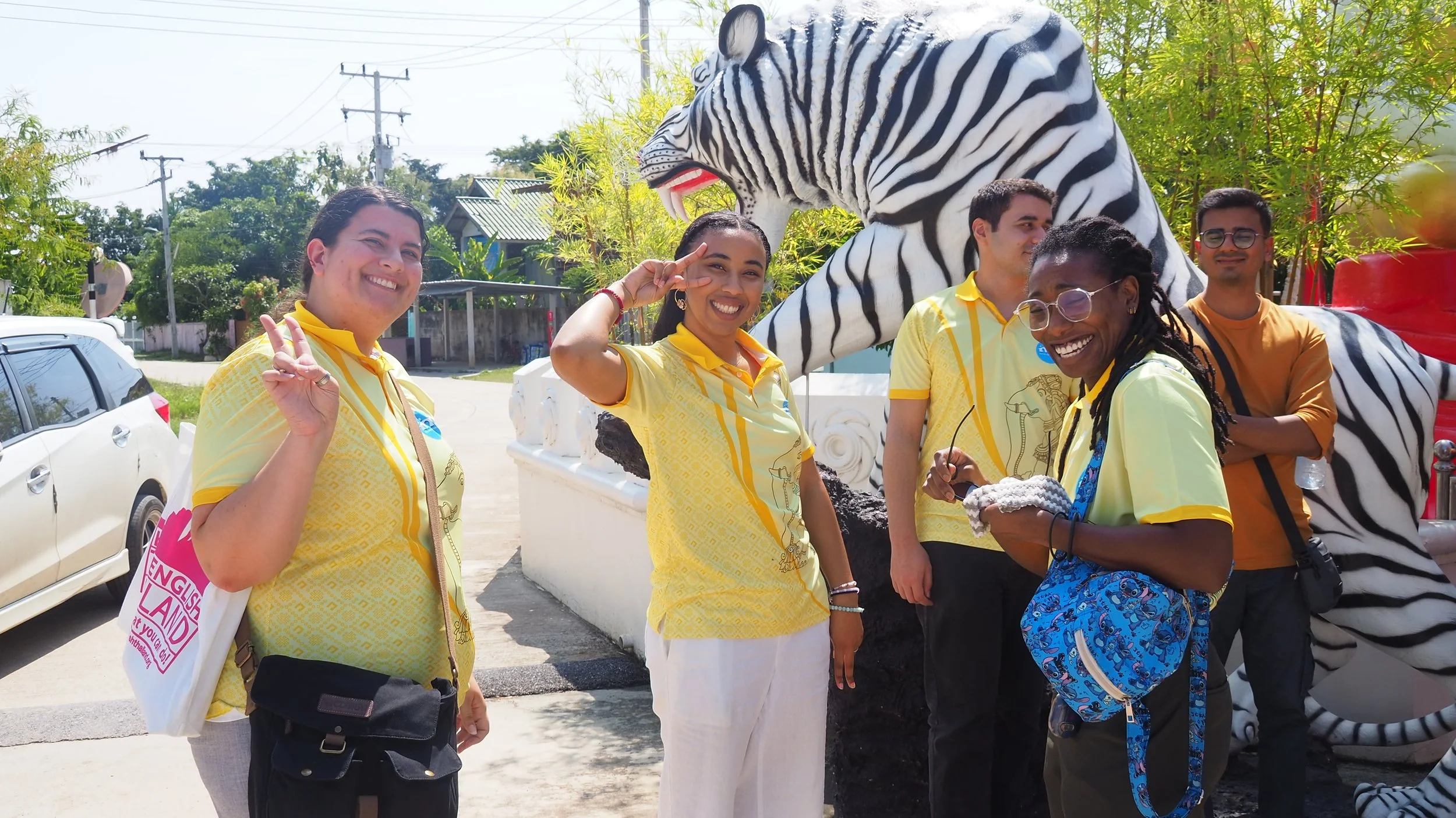 Group of five smiling KET Teachers standing outdoors, posing in front of a zebraprint statue, with green trees and a clear sky in the background.