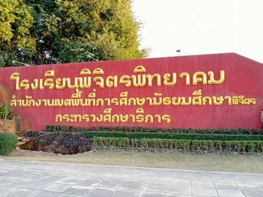 Kids English Thailand Image-Red wall with yellow Thai text, surrounded by greenery.