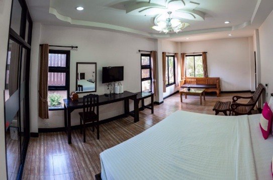 Kids English Thailand Image-Spacious hotel room with a large bed, wooden furniture, multiple windows, and a flat-screen TV.