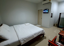Kids English Thailand Image-A small, minimally furnished hotel room with a double bed, a wall-mounted TV, and a doorway.