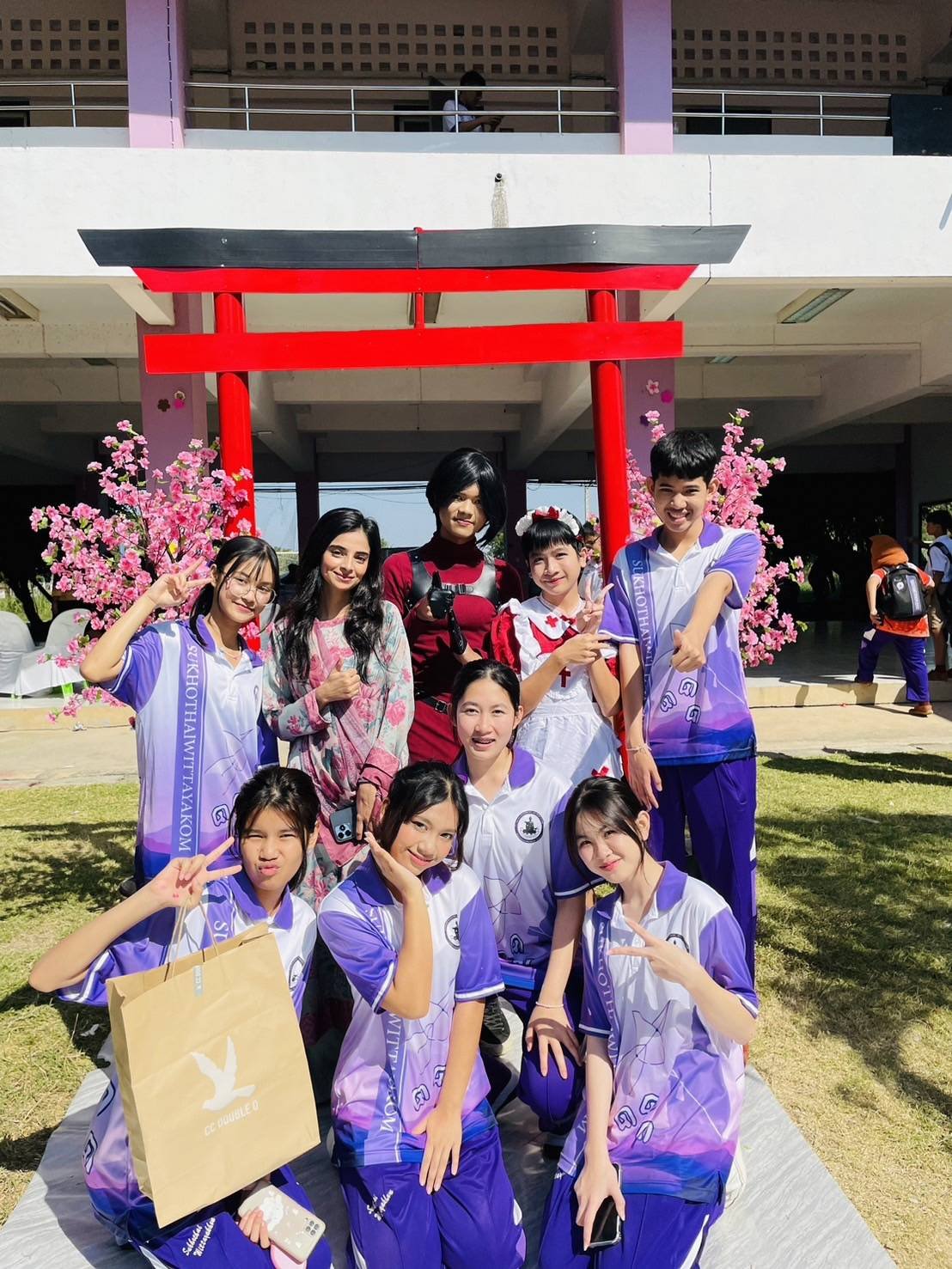 Group of young students and Kids English Thailand teachers posing at a cultural event with a red traditional Japanese torii gate and pink cherry blossom decorations in the background.