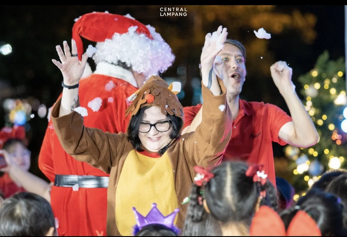 Kids English Thailand teachers dressed in Christmas and holiday costumes celebrating at a festive outdoor event, with Christmas lights in the background.