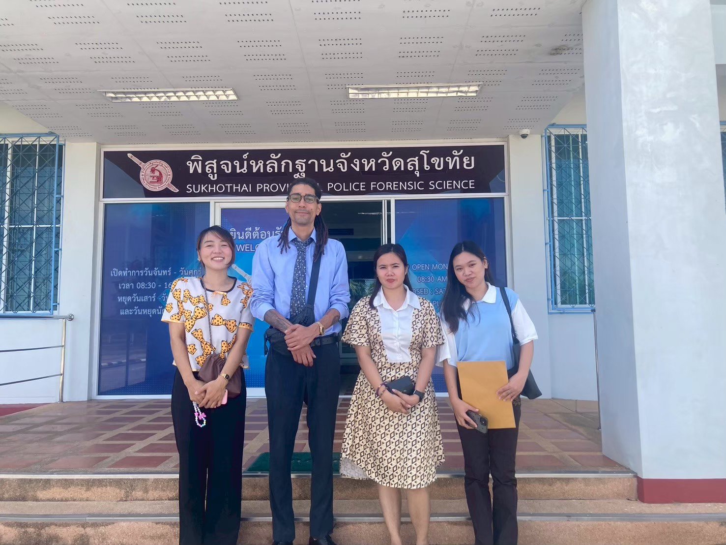 Four people from Kids English Thailand standing in front of Sukhothai Province Police Forensic Science building entrance