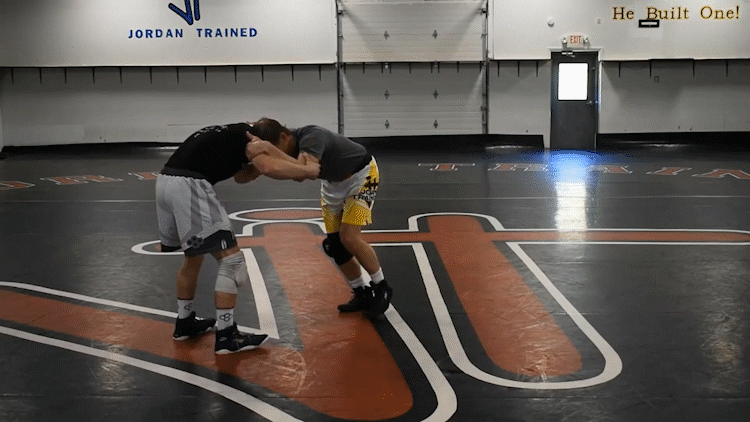 Jordan demonstrating the entry to the JTSLS. Note the tie-up (right arm collar tie, left arm inside tie), set-up (circling away from target leg and pulling down on the opponent’s head just prior to the shot), and the level change + angle knee drop p…