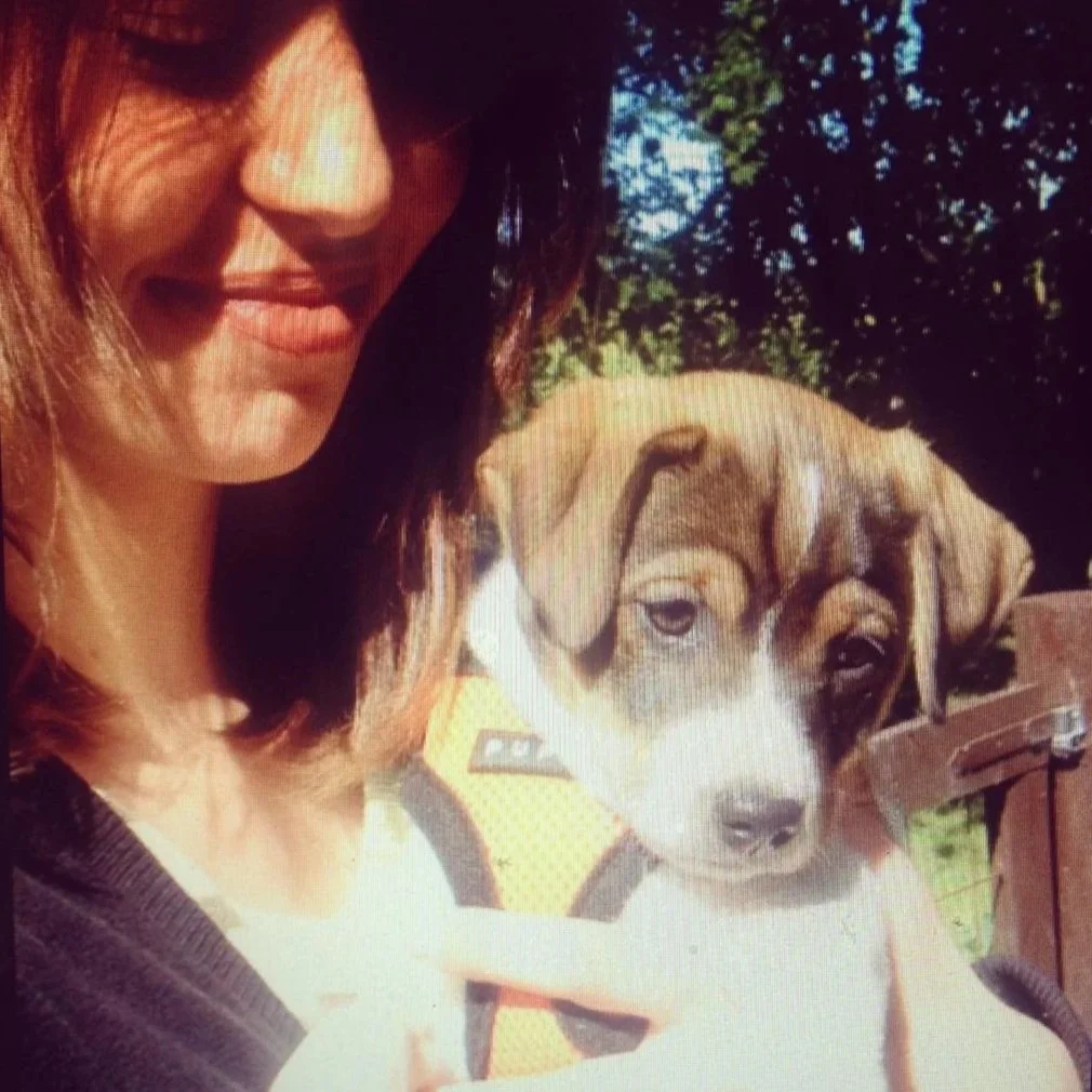 Eine Frau und ein Welpe im Freien, umgeben von Bäumen.