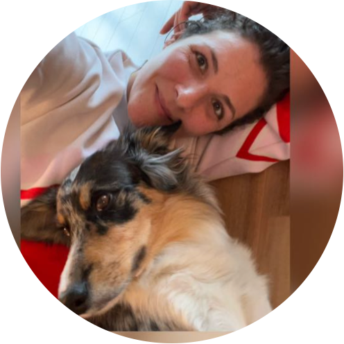 Frau liegt lächelnd auf dem Boden mit einem Hund im Vordergrund. Der Hund hat ein buntes Fellmuster und liegt nah bei ihr.